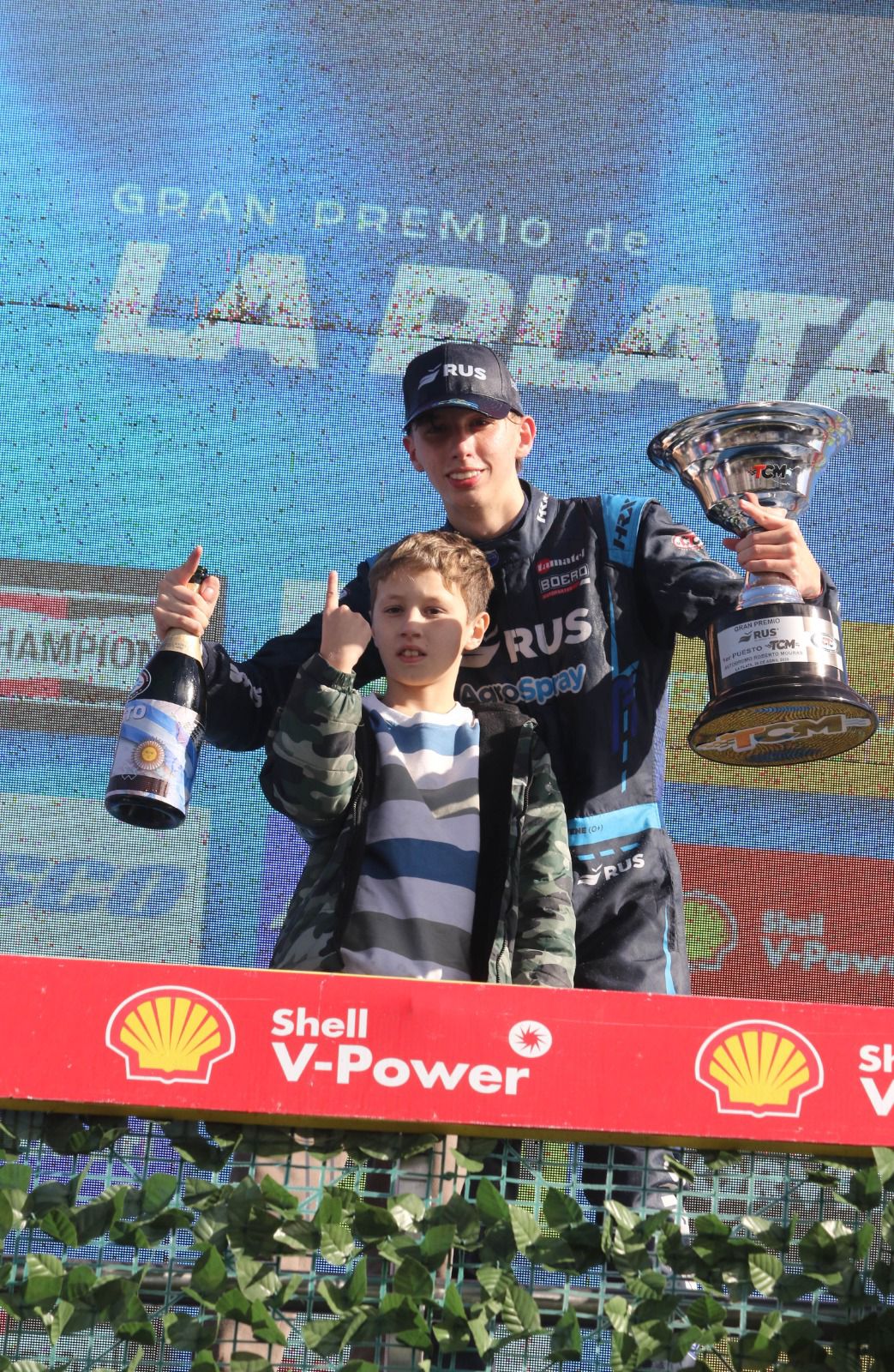 Thiago Falivene festejando en el podio con el trofeo, junto a su hermano